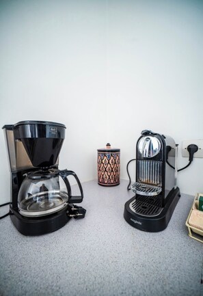 Two coffee makers on a countertop, a patterned mug, and a small box.