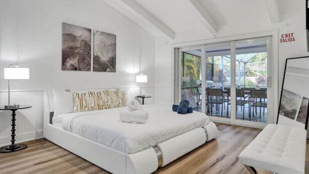 A modern hotel room with a large bed, a sitting area with a chair, a glass door leading to an outdoor patio, and artwork on the walls.