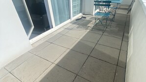 En balkong med kakelgolv, en grön hopfällbar stol och ett fönster med persienner.