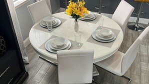 Ein runder Esstisch mit weißen Stühlen, eine Vase mit gelben Blumen und klarem Glas.