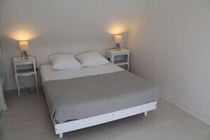 A single-bed room with a white bed, two bedside tables with lamps, and a light switch on the wall. - Peaceful house with garden 3 minutes from the beach (Combrit)