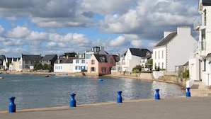 Une vue sur le front de mer, avec des bâtiments le long de la côte, une étendue d’eau calme et un ciel dégagé.