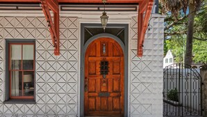 Een gebouw met een opvallende houten deur, een raam met rode omlijsting, en een muur met een geometrisch patroon.