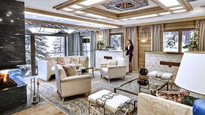 A spacious living area with a fireplace, comfortable seating, and large windows offering a view of snowy trees. - LYS MARTAGON (Courchevel)