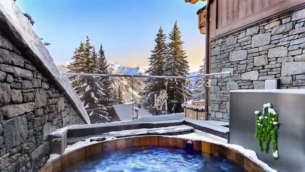 A hot tub with a stone wall and a view of snow-covered mountains. - LYS MARTAGON (Courchevel)
