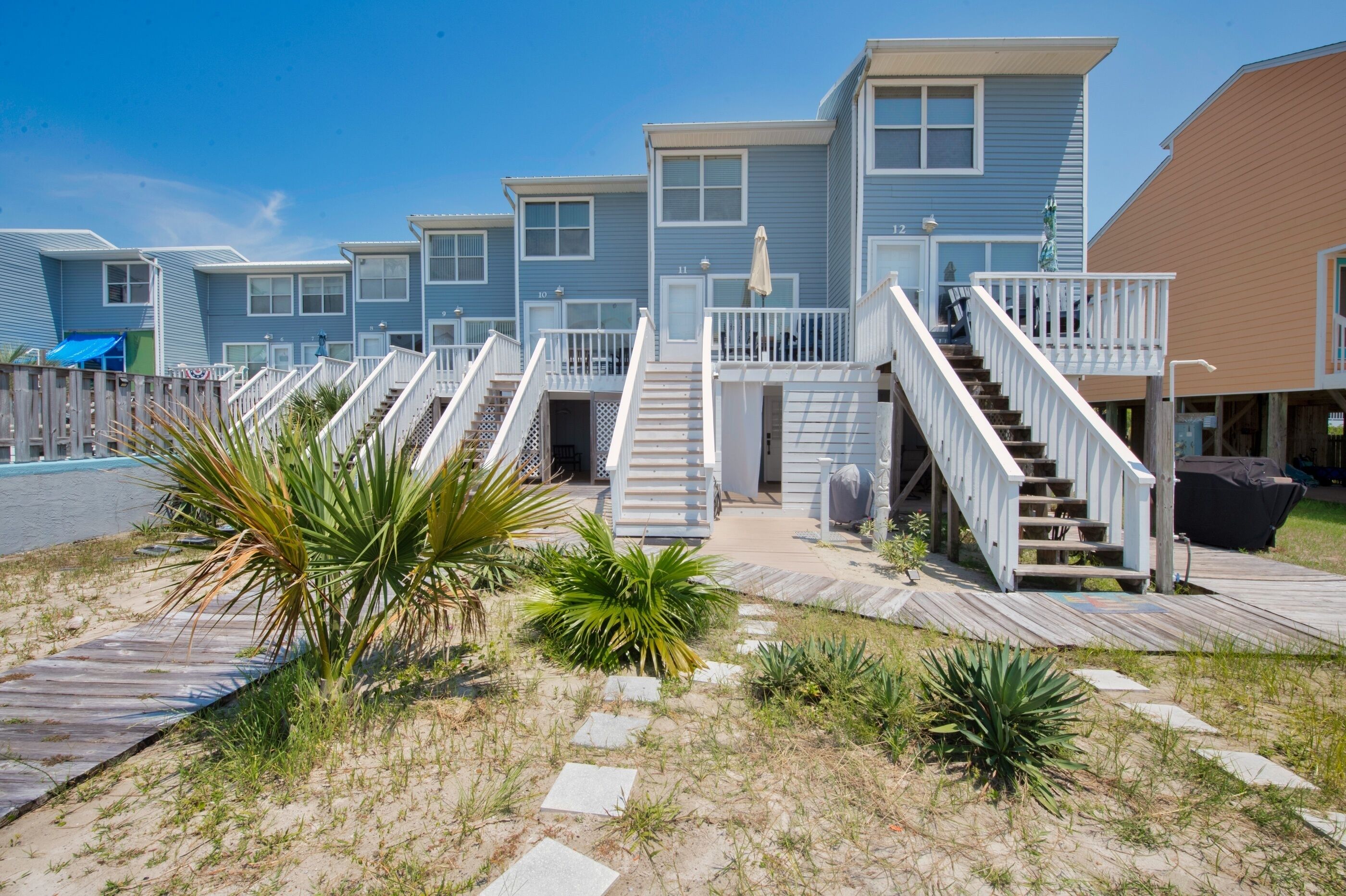 A row of beachside cabins with wooden decks and stairs leading to the entrance.