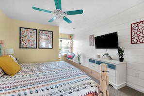 Ein Schlafzimmer mit Bett, Deckenventilator, Fernseher, Kommode und Fenster.