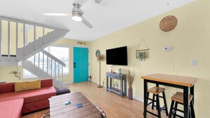 Ein Wohnzimmer mit Couch in Rot, einem Holztisch, einer türkisfarbenen Tür, einem Fernseher an der Wand und einer Treppe.