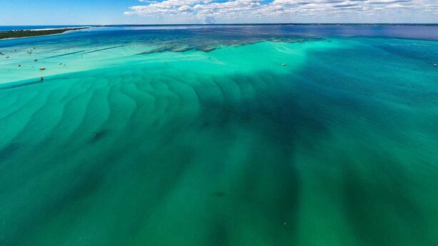 Eine Vogelperspektive auf eine Küstenregion mit klarem türkisblauem Wasser und einem Sandstrand.