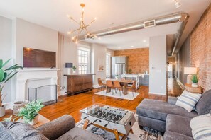 A modern living room with a foosball table, a fireplace, and a kitchen in the background. - Relaxing, Boho Chic 2B 2Bath Downtown City View Condo (Cincinnati)