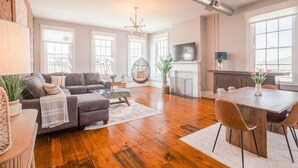 Ein geräumiges Wohnzimmer mit Sofa, Couchtisch und Essbereich. Es gibt einen Hängekorbsessel und einen Kamin.