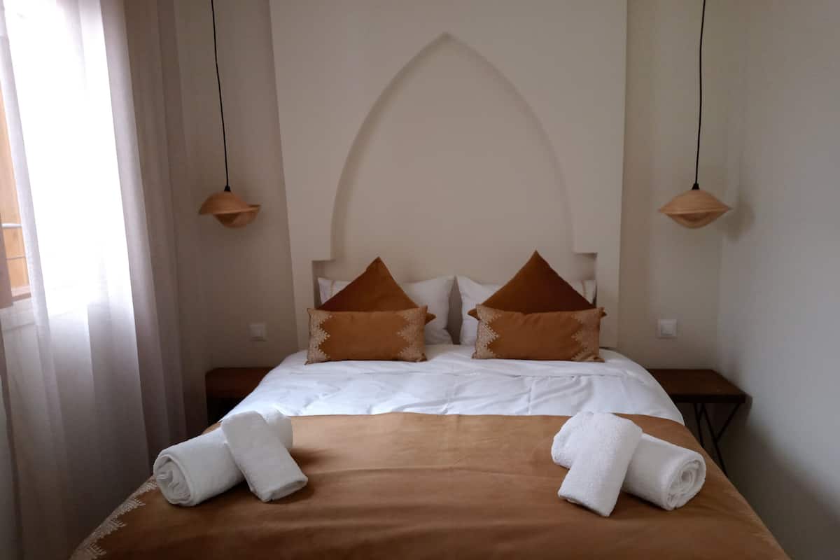 A hotel room with a large bed, brown and white bedding, two nightstands, and pendant lights.