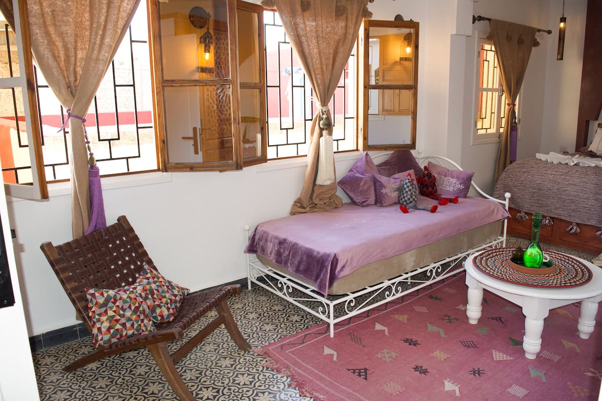 A bedroom with a bed, a chair, a table, and a window with curtains.