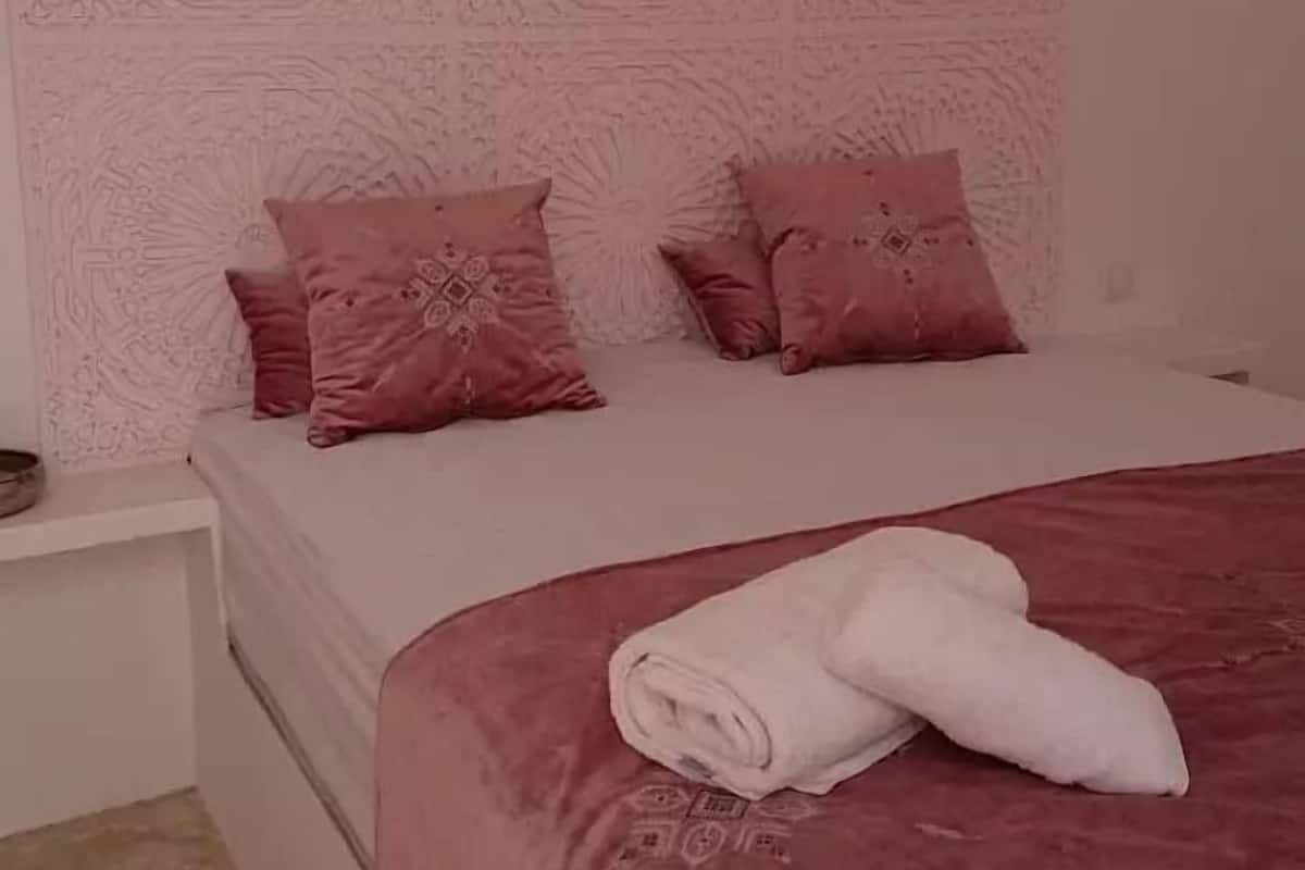 A bedroom with a patterned headboard, two pillows, a neatly folded towel, and a hanging light fixture.
