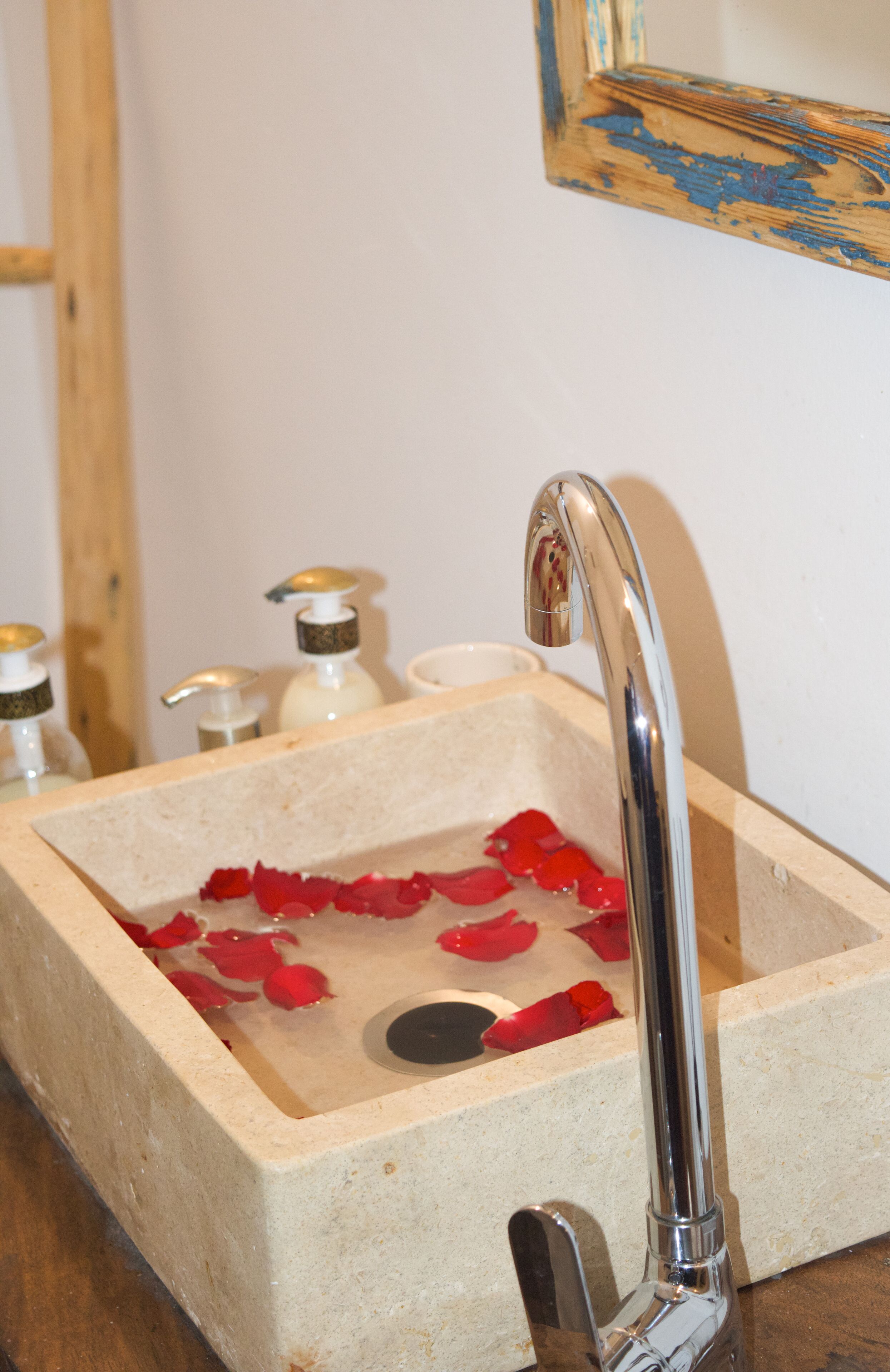 A bathroom sink with rose petals, a mirror, and soap dispensers.