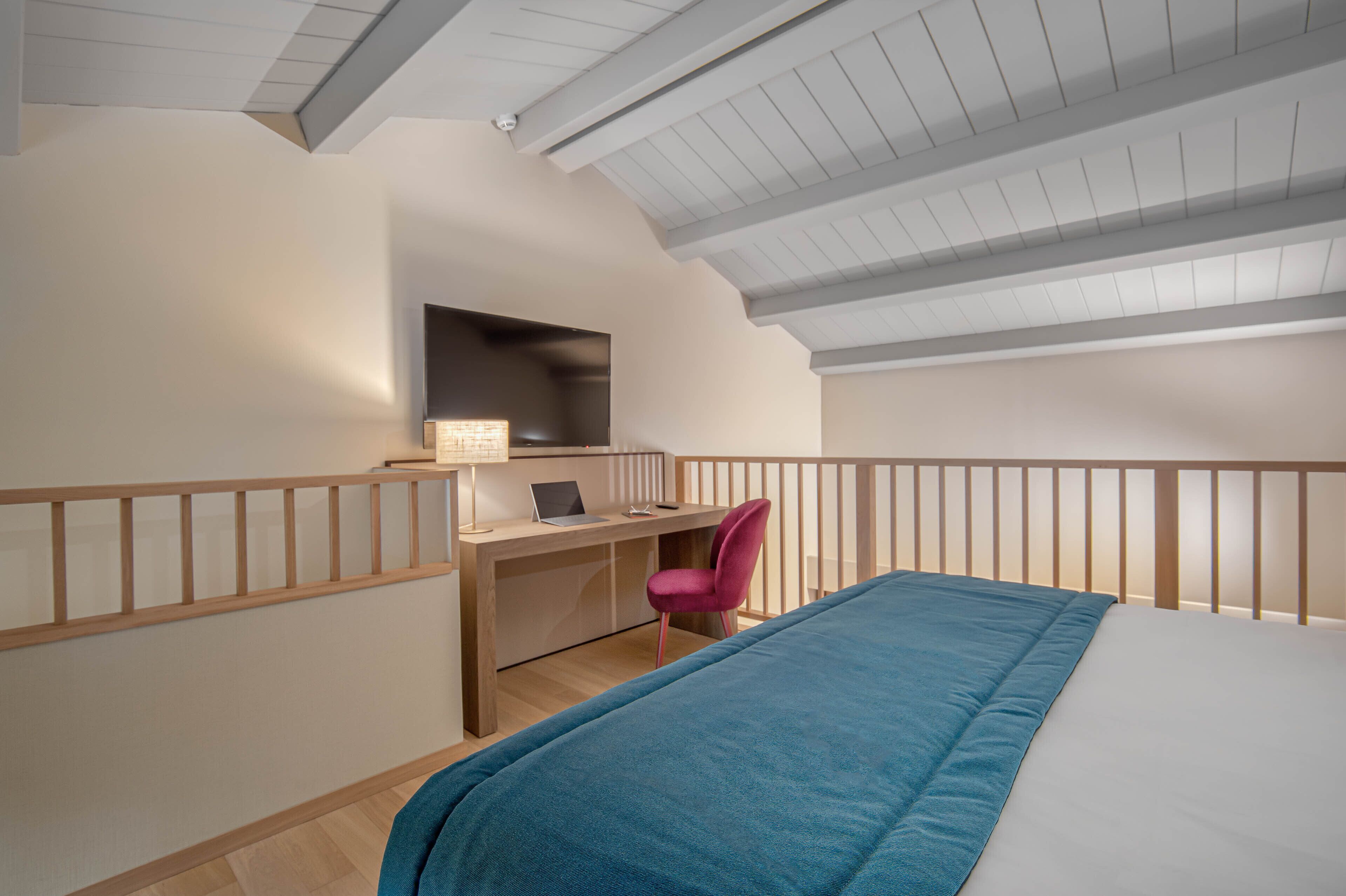 A bedroom with a bed, a desk with a chair, and a television.