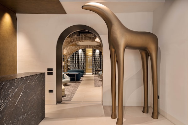 A modern interior with a reception desk, a large golden sculpture, and a view into a room with a blue sofa and a patterned curtain.
