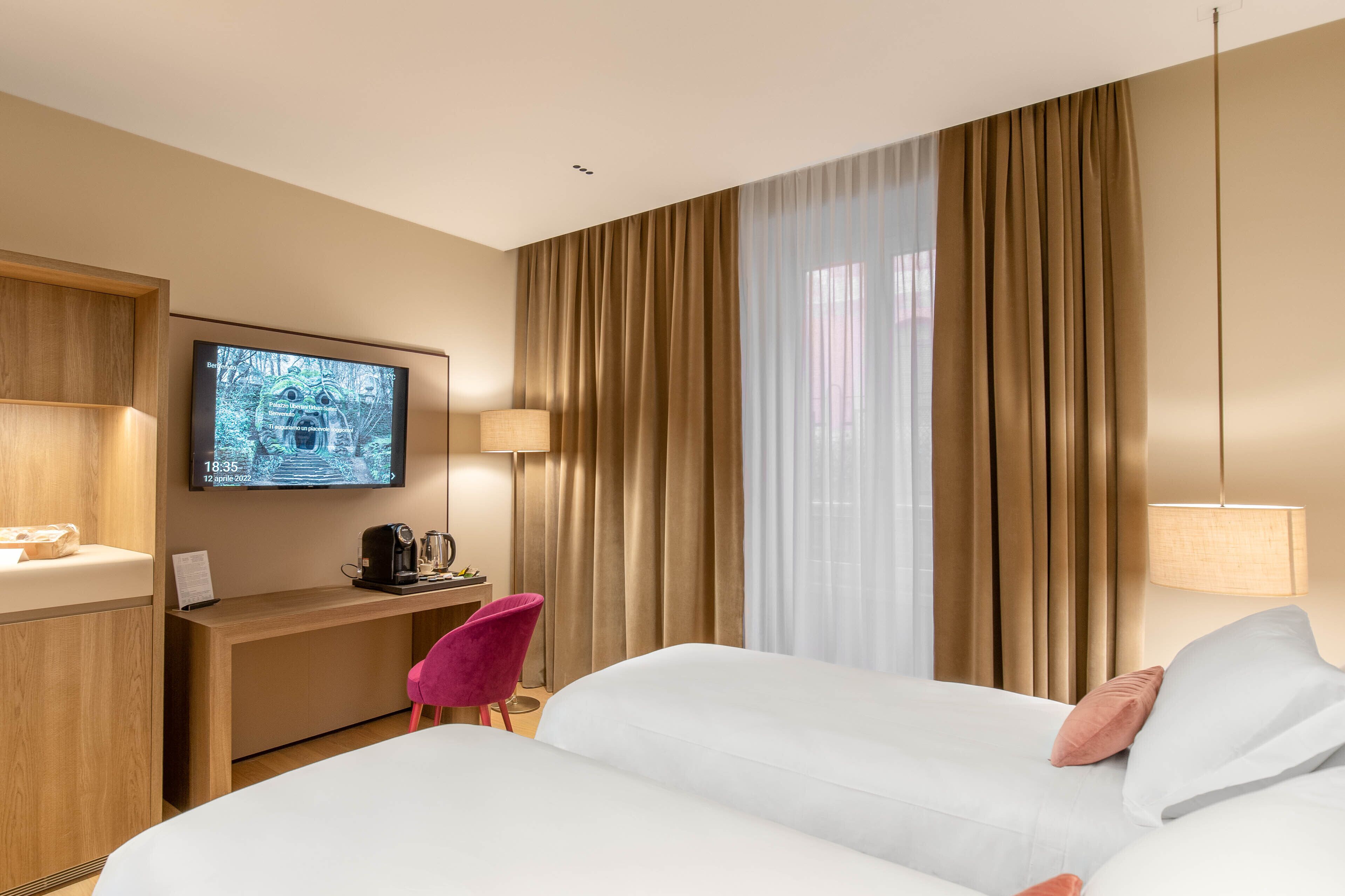 Ein Hotelzimmer mit Bett, Schreibtisch mit Computer, Stuhl, Fernseher und Vorhängen.