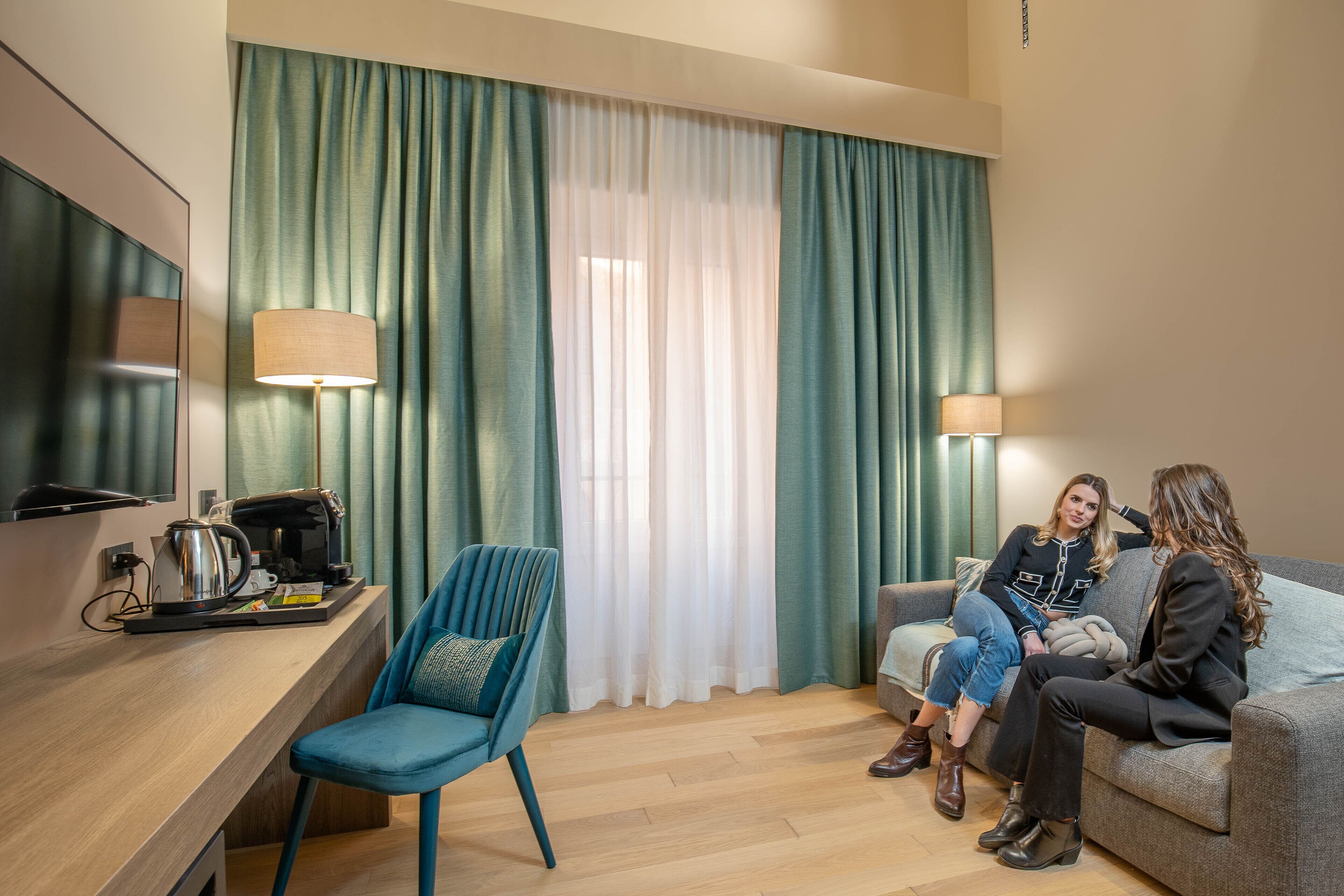 Una camera d'albergo moderna con una scrivania in legno, una sedia blu, un divano e una televisione.