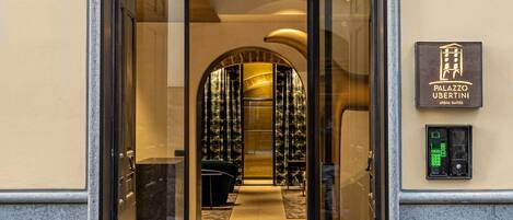 Entrada de hotel con puerta de vidrio, mostrador de recepción y letrero con el nombre del hotel.
