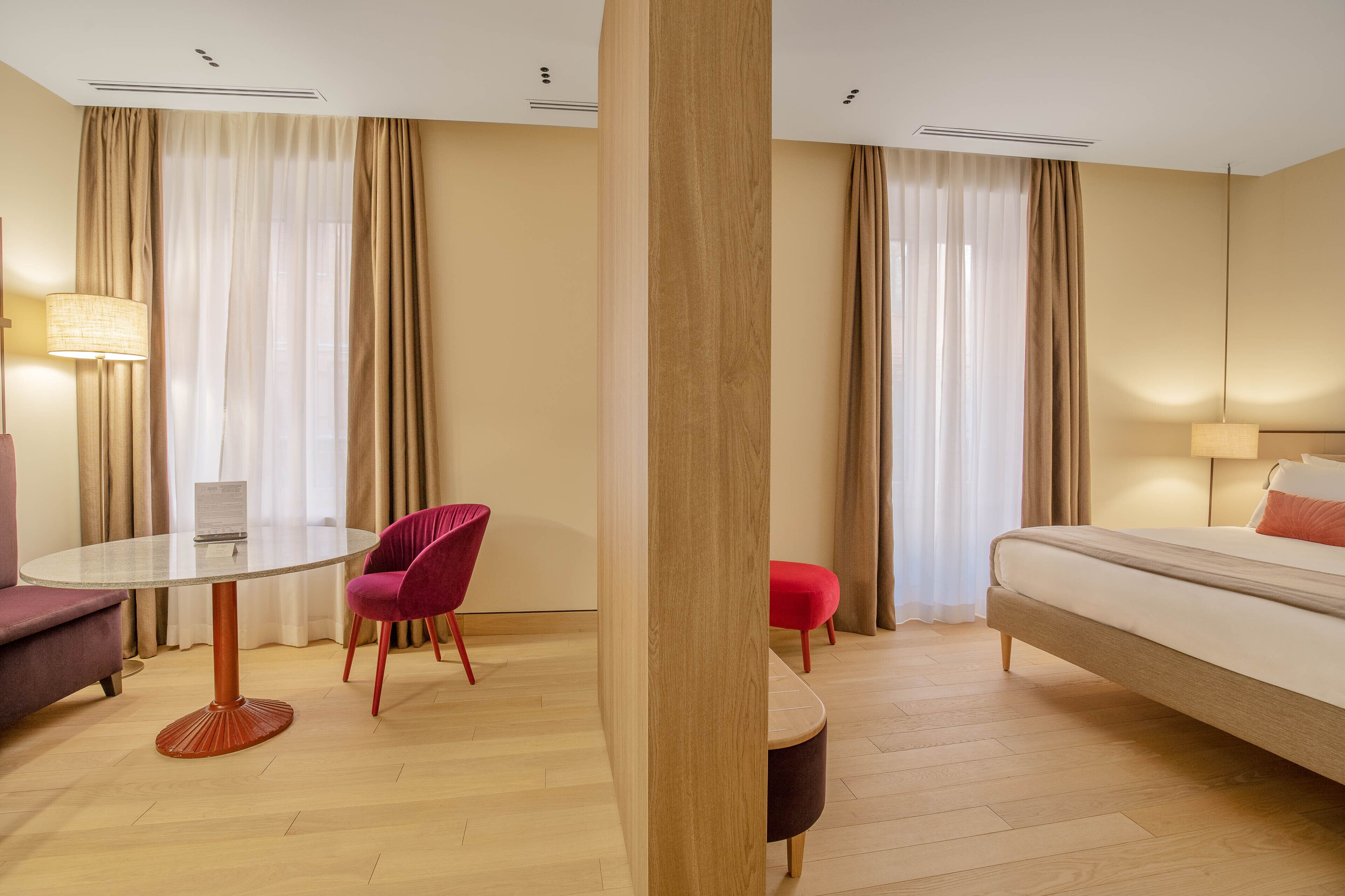 A hotel room with a round table, two chairs, a sofa, a bed, and a small ottoman.