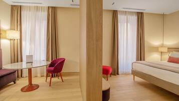 A hotel room with a round table, two chairs, a sofa, a bed, and a small ottoman.
