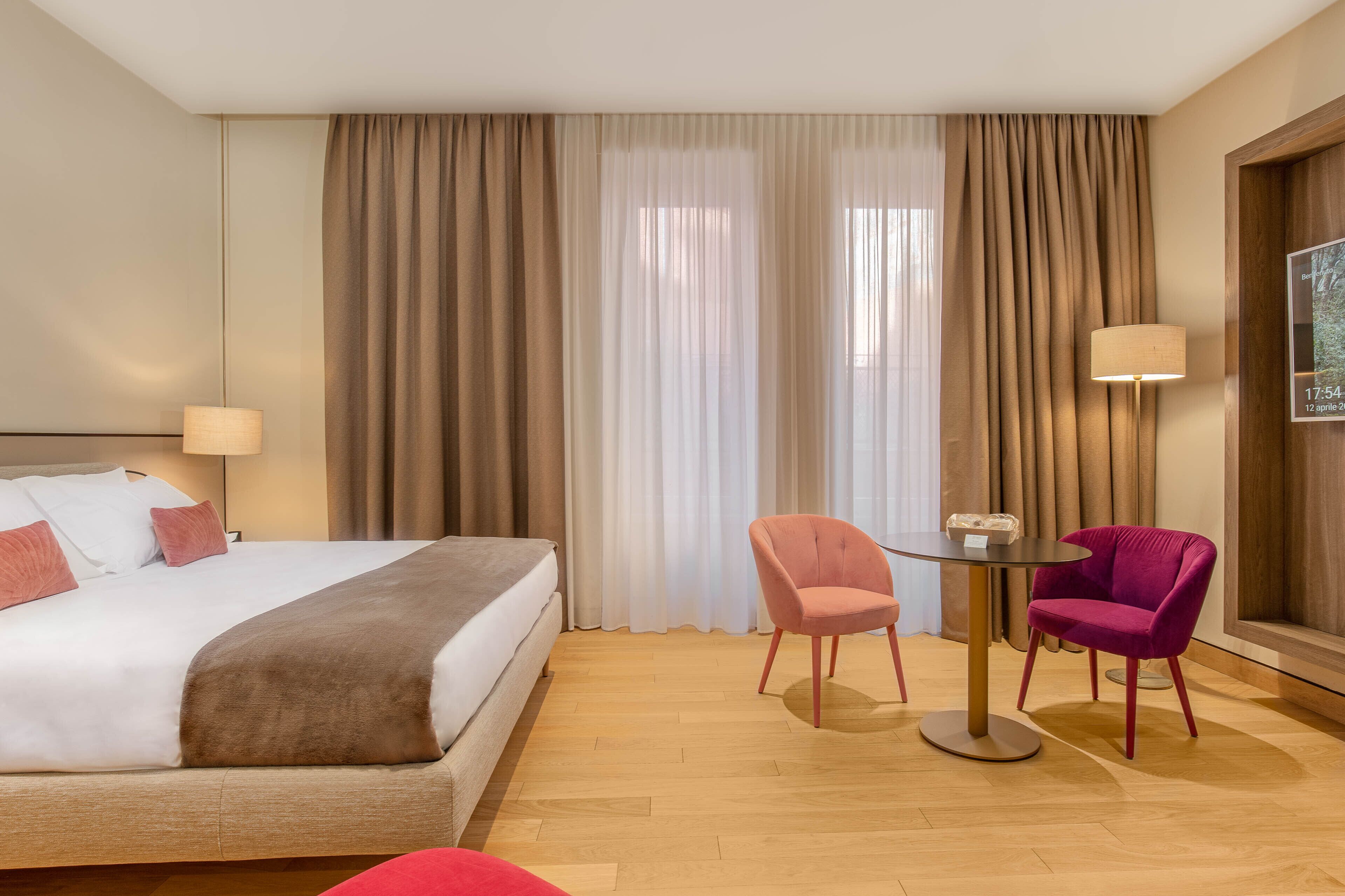 A hotel room with a bed, two chairs, a small table, and a lamp.