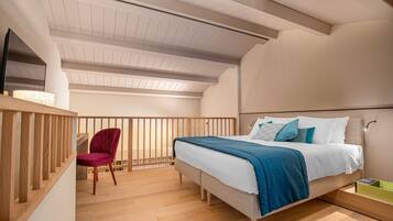 Un dormitorio con cama, una silla, suelo de madera y techo inclinado.