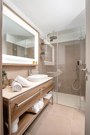 A modern bathroom with a glass-enclosed shower, a large mirror, and a wooden vanity with a sink and towel rack.