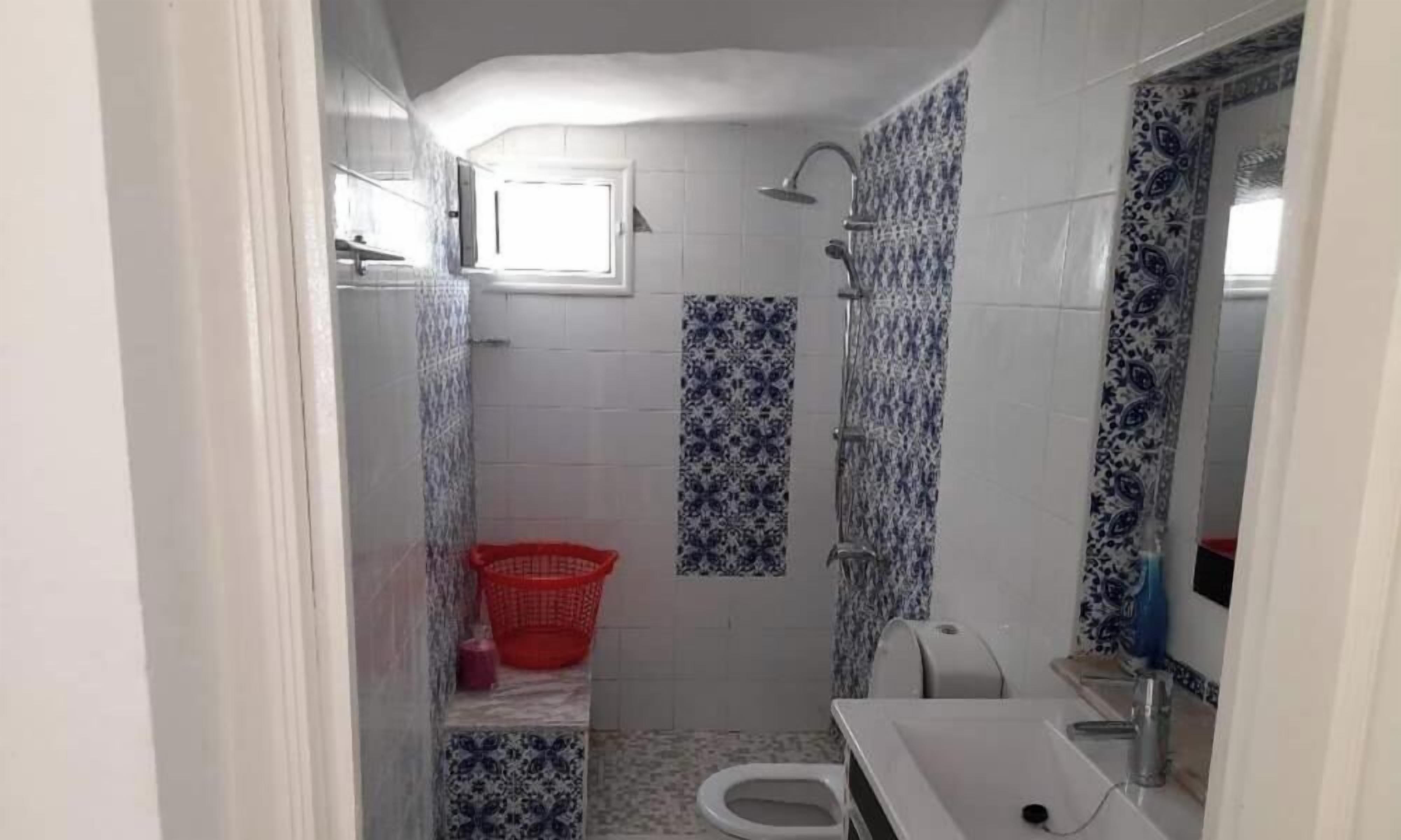 Une petite salle de bain avec des toilettes, un lavabo, une douche et un panier à linge rouge.