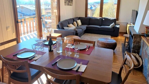 Ein Essbereich mit einem Holztisch, gedeckten Plätzen für vier Personen, einer dunkelgrauen Couch und einem Kamin.