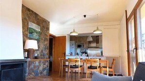 Ein gemütliches Wohnzimmer mit Kamin, ein Essbereich mit Holzsesseln und eine Küche im Hintergrund.