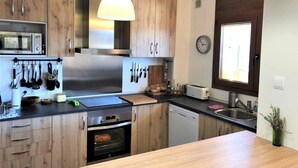 Eine moderne Küche mit Holzschränken, einem eingebauten Ofen, einer Mikrowelle und einer Pendelleuchte.