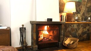 Ein gemütlicher Raum mit Kamin aus Stein, Holzboden und einer Lampe auf einem Tisch.