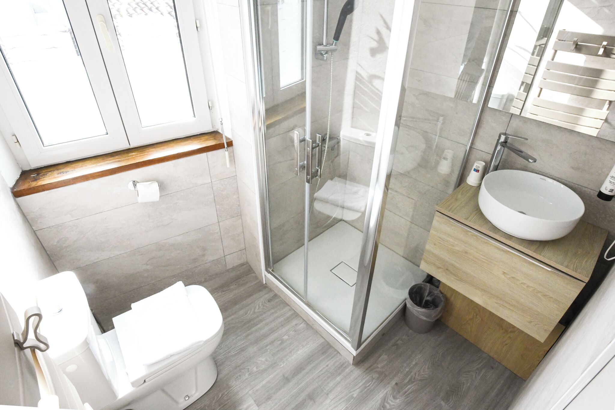 A modern bathroom with a glass-enclosed shower, a white toilet, and a wooden vanity with a sink.