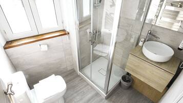 Un baño moderno con ducha de vidrio, inodoro blanco y tocador de madera con lavabo.