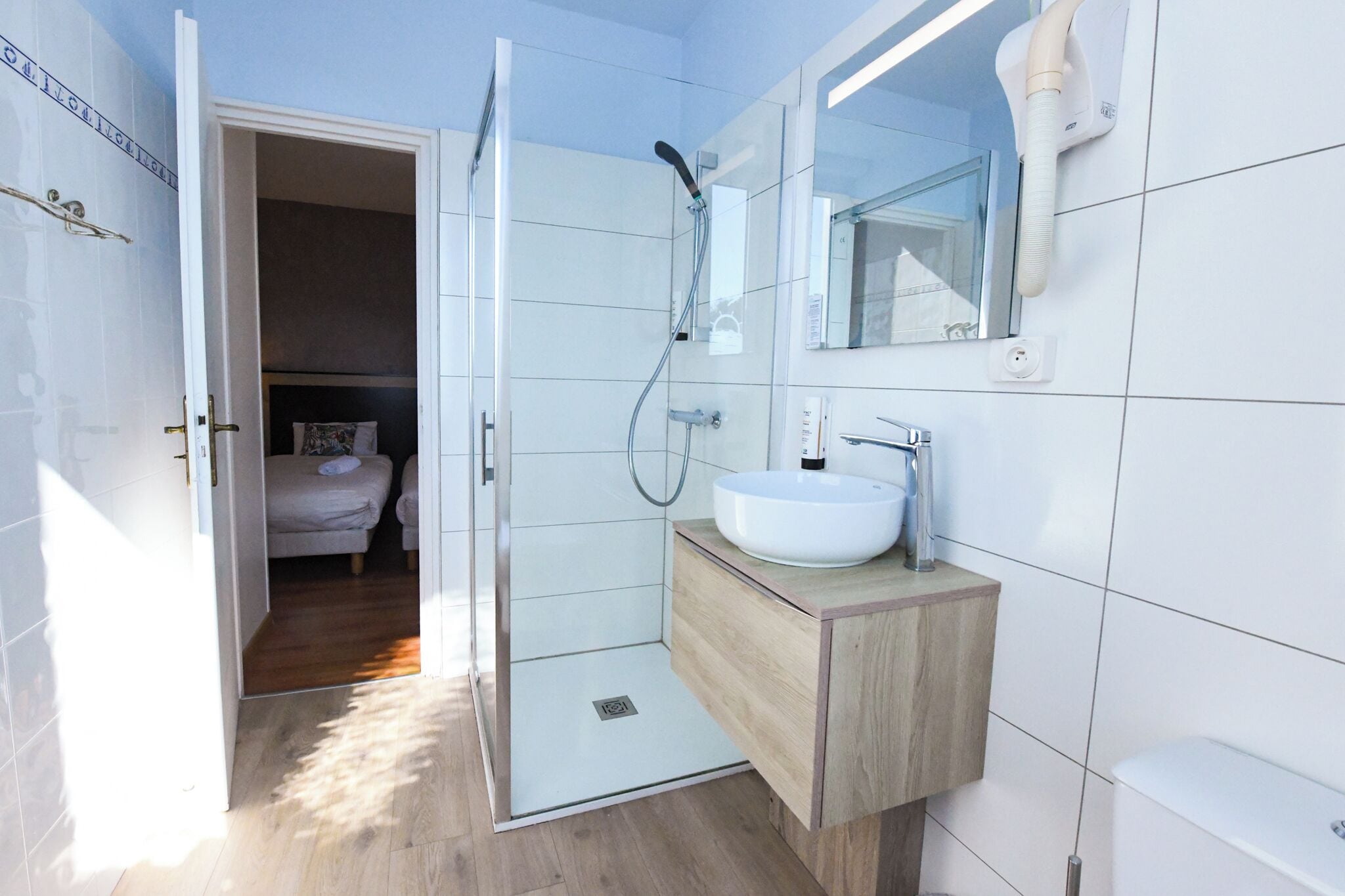 Un baño moderno con ducha de mampara de vidrio, un lavabo blanco y un mueble de tocador de madera.