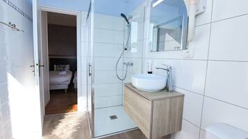 A modern bathroom with a glass-enclosed shower, a white sink, and a wooden vanity.