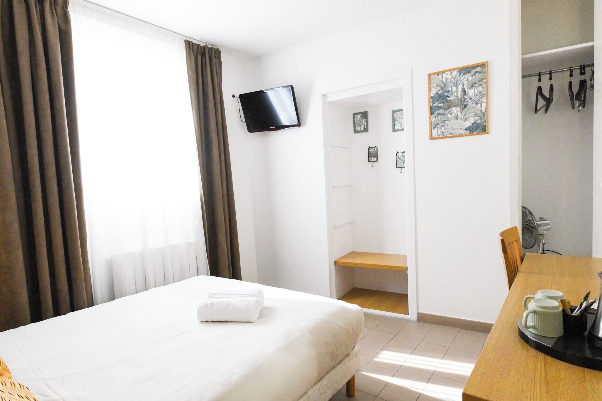 A hotel room with a bed, a TV mounted on the wall, a desk with a coffee maker, and a door leading to a bathroom.