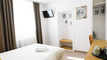 A hotel room with a bed, a TV mounted on the wall, a desk with a coffee maker, and a door leading to a bathroom.