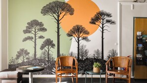 A room with two wooden chairs, a small table, and a wall mural depicting trees and a sun. -  Hotel le Coureau (Saint-Trojan-les-Bains)