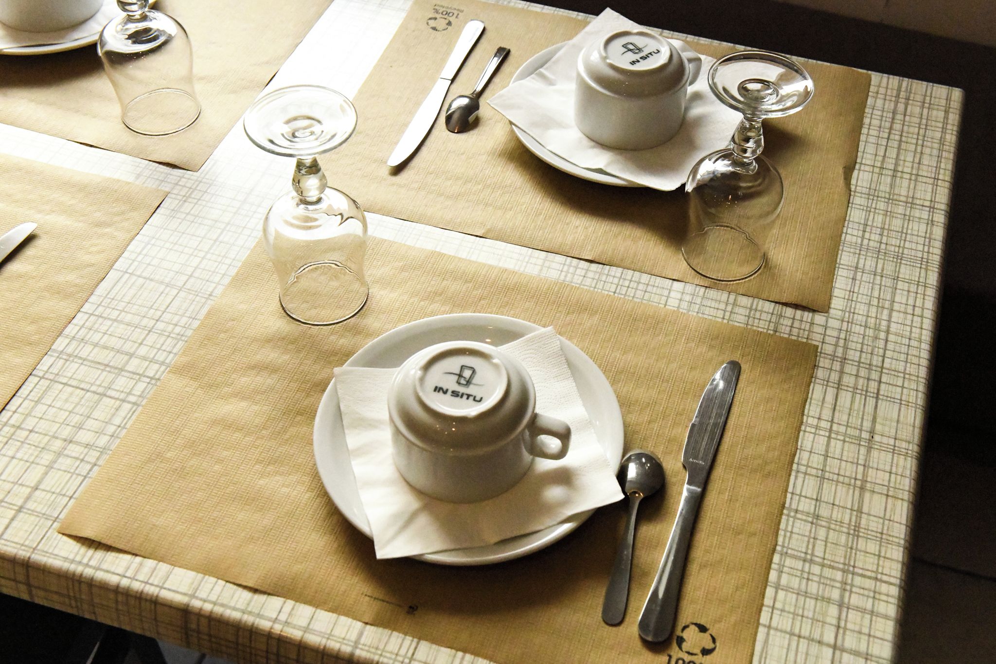 A table set with a teapot, cups, a glass, and cutlery on a checkered tablecloth.