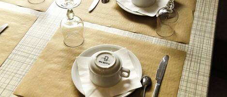 A table set with a teapot, cups, a glass, and cutlery on a checkered tablecloth.