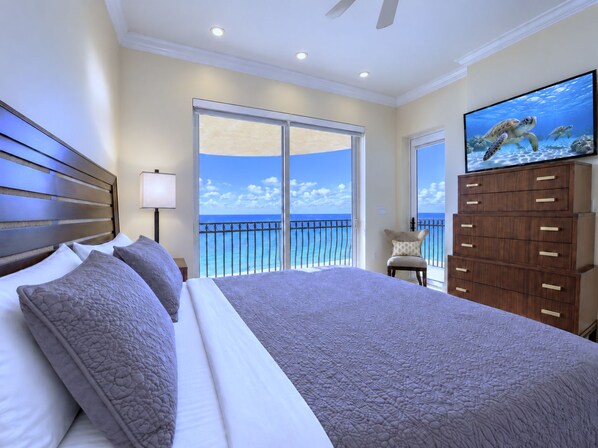 A bedroom with a large bed, a television, a nightstand, and a view of the ocean.