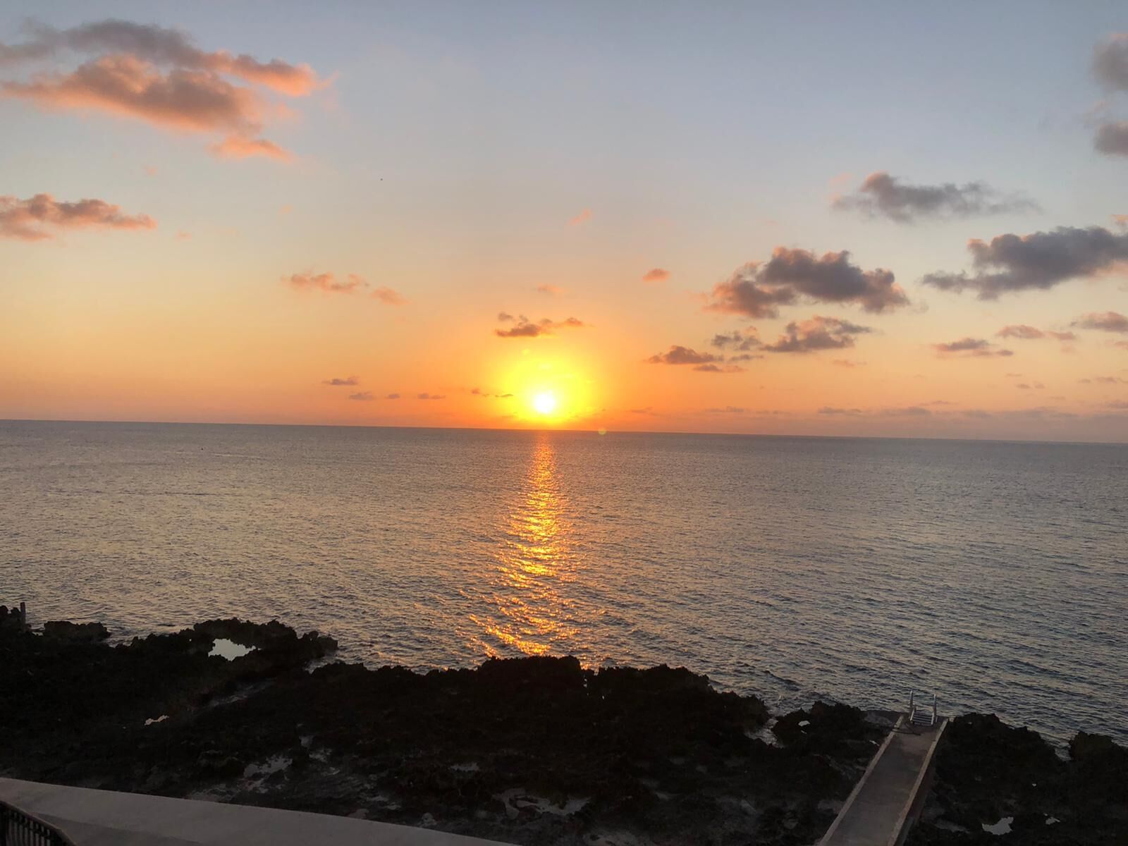 A sunset over the ocean with a rocky shoreline.