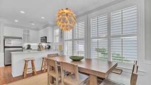 Una cocina moderna con armarios blancos, una isla central y una zona de comedor con sillas y taburetes de madera.