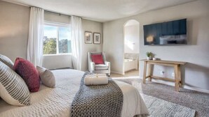 Une chambre avec un grand lit, une chaise, une télévision et une petite table.