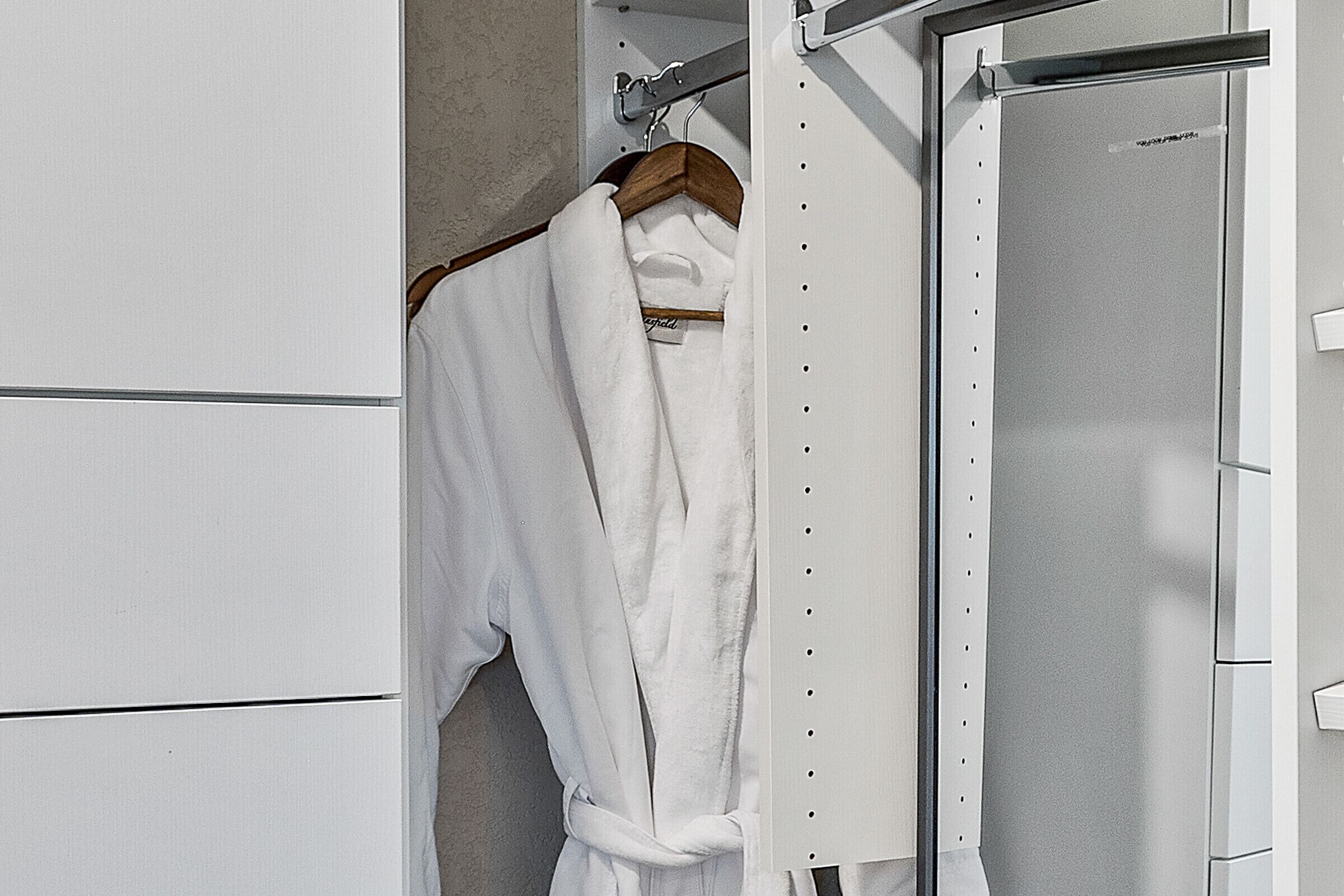 A white robe hanging on a wooden hanger in a closet with a metallic door.