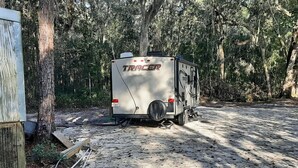 A white RV with 'TRACER' written on the side parked in a wooded area.