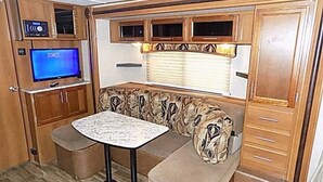 A compact RV interior with a kitchenette, a seating area with a table, and a television.
